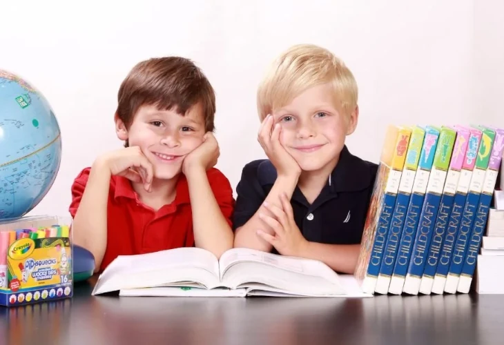 két kisfiú egy asztalnál ülve könyökölnek, mosolyognak